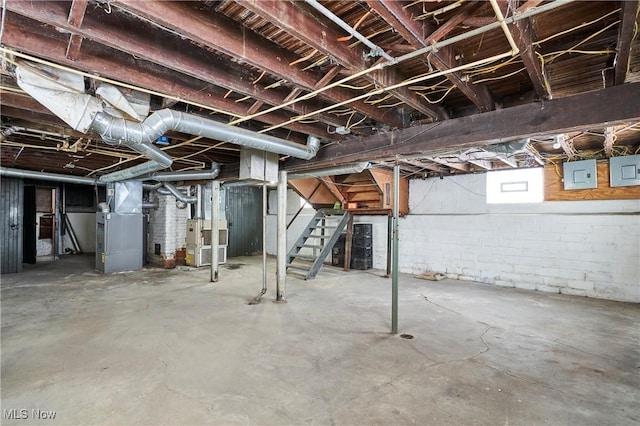 basement featuring electric panel, stairway, and heating unit