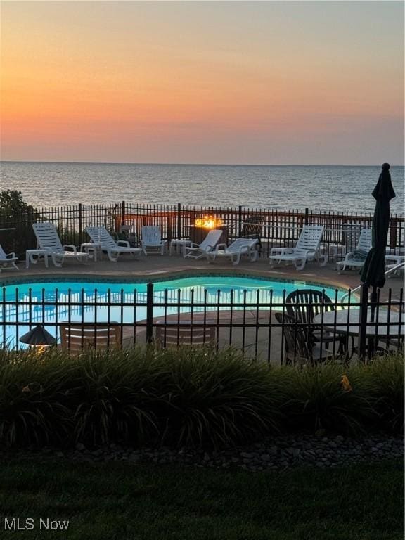 pool with a patio area, a water view, and fence