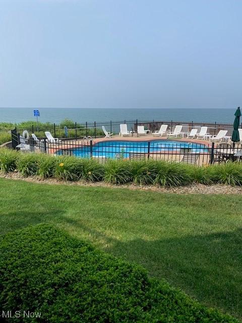 community pool with a yard, a water view, and fence