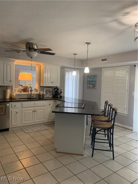 kitchen featuring black electric cooktop, a sink, visible vents, dishwasher, and dark countertops