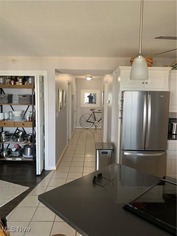 kitchen featuring black electric stovetop, light tile patterned flooring, baseboards, white cabinets, and freestanding refrigerator