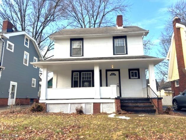 traditional style home with a chimney, a porch, and a front yard