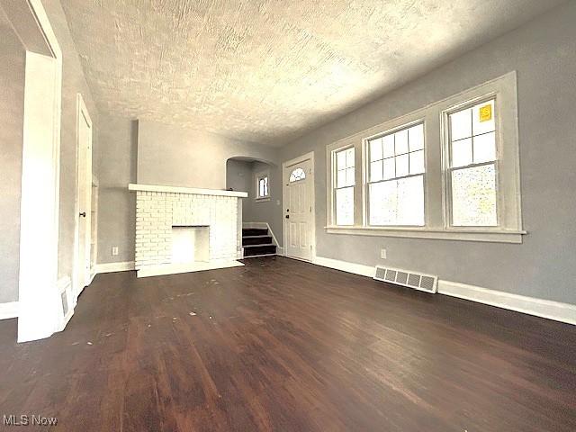 unfurnished living room featuring a fireplace, visible vents, wood finished floors, baseboards, and stairs