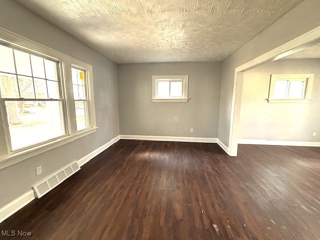 empty room with visible vents, dark wood finished floors, and baseboards