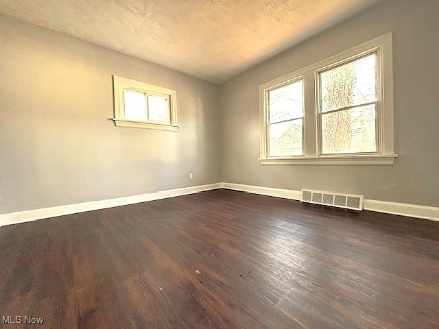 empty room featuring dark wood-style floors, visible vents, and baseboards