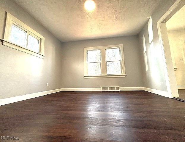 empty room with dark wood-style flooring, visible vents, a textured ceiling, and baseboards