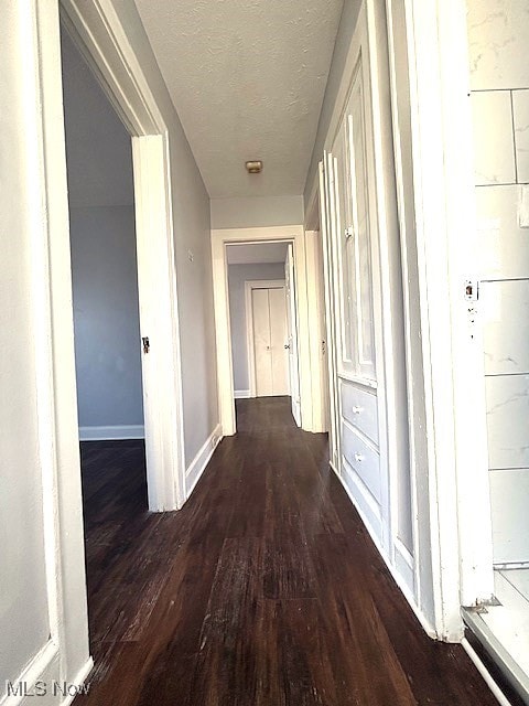 hallway with a textured ceiling, baseboards, and wood finished floors