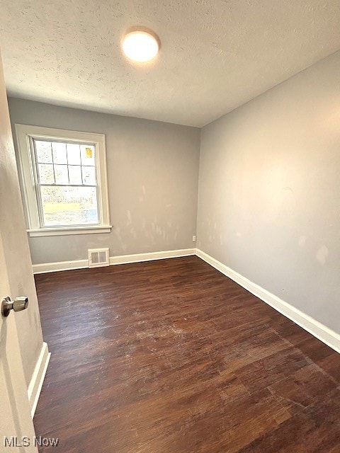 empty room with baseboards, visible vents, dark wood finished floors, and a textured ceiling