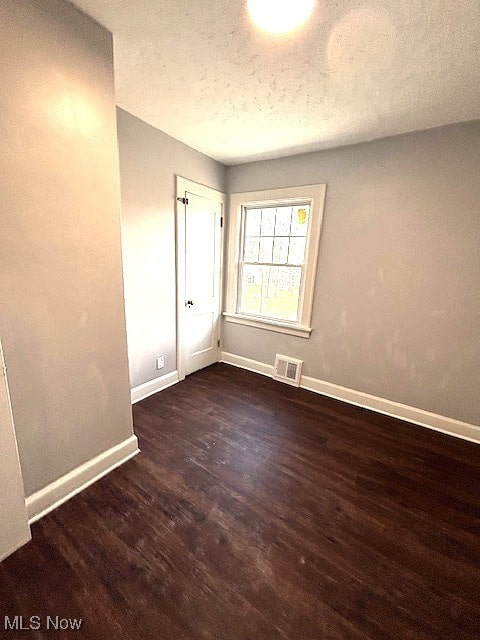 unfurnished room featuring baseboards, a textured ceiling, visible vents, and dark wood-type flooring