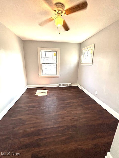 spare room with dark wood-style floors, ceiling fan, visible vents, and baseboards