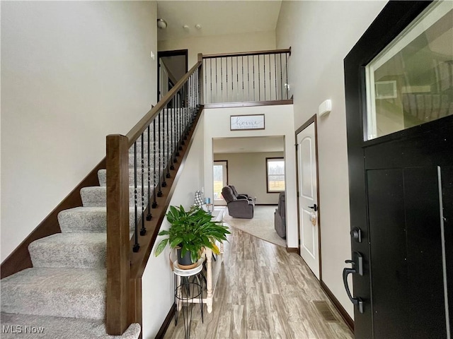 interior space featuring wood finished floors, visible vents, a towering ceiling, stairs, and baseboards