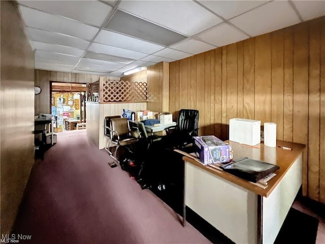 carpeted office space featuring wood walls and a drop ceiling