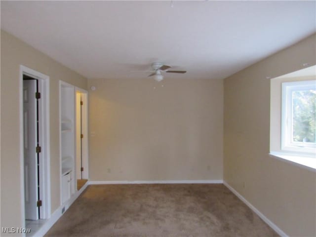 carpeted spare room with a ceiling fan and baseboards