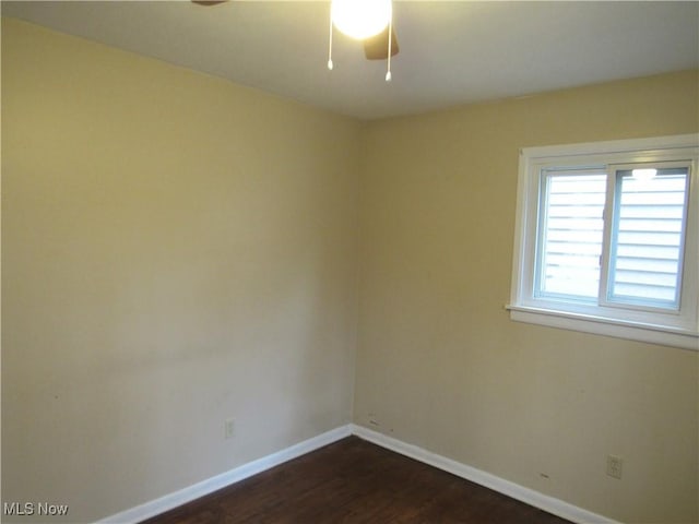 empty room featuring dark wood-style flooring, a ceiling fan, and baseboards