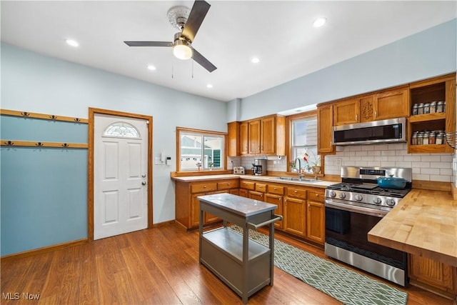 kitchen with butcher block counters, dark wood-type flooring, stainless steel appliances, open shelves, and a sink