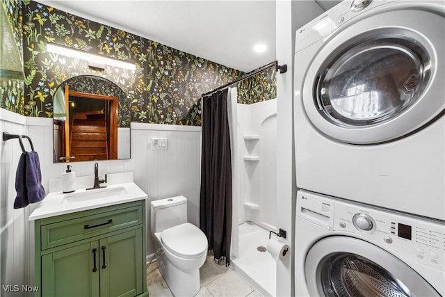 full bathroom with a wainscoted wall, stacked washer and dryer, toilet, a shower stall, and wallpapered walls