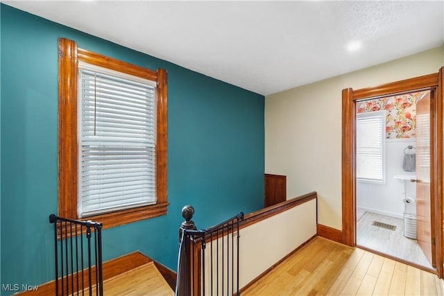 hall with plenty of natural light, baseboards, wood finished floors, and an upstairs landing