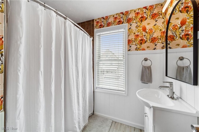 bathroom featuring curtained shower, wainscoting, vanity, and wallpapered walls