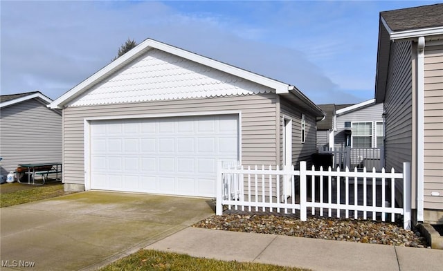 exterior space featuring concrete driveway, fence, an outdoor structure, and an attached garage