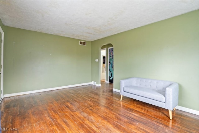 sitting room featuring arched walkways, visible vents, a textured ceiling, baseboards, and hardwood / wood-style flooring