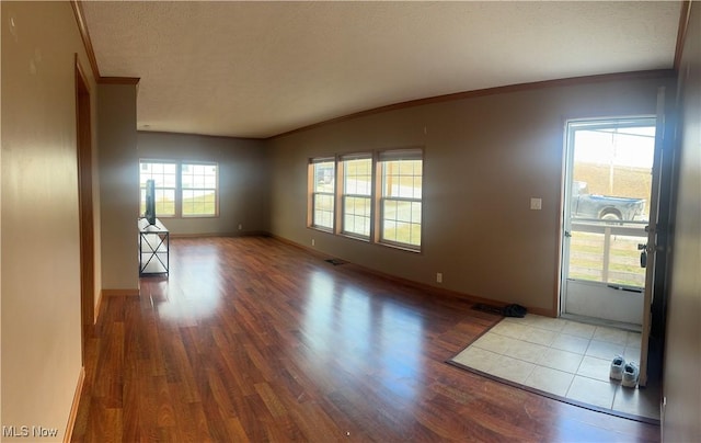 interior space with baseboards, a textured ceiling, ornamental molding, and wood finished floors