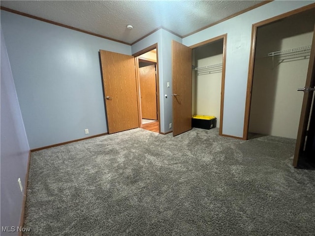 unfurnished bedroom with a textured ceiling, carpet floors, ornamental molding, and multiple closets