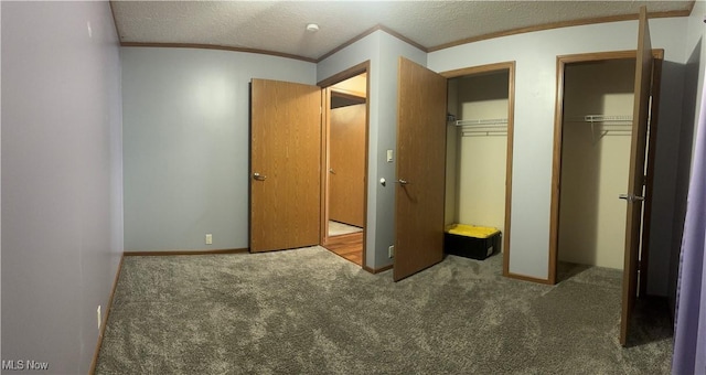 unfurnished bedroom featuring carpet floors, ornamental molding, a textured ceiling, and two closets