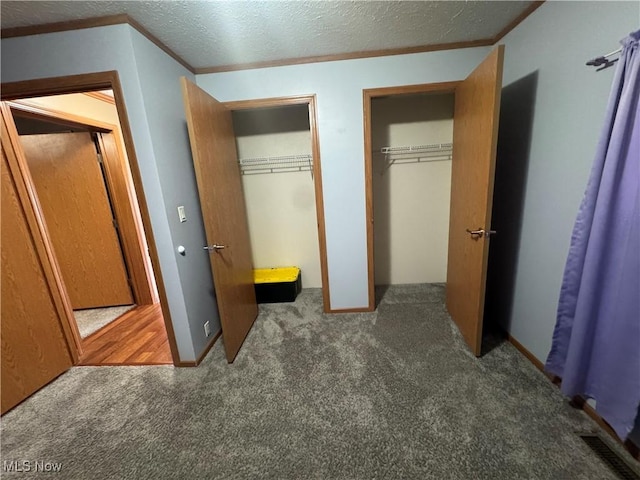 unfurnished bedroom with visible vents, ornamental molding, a textured ceiling, carpet flooring, and multiple closets