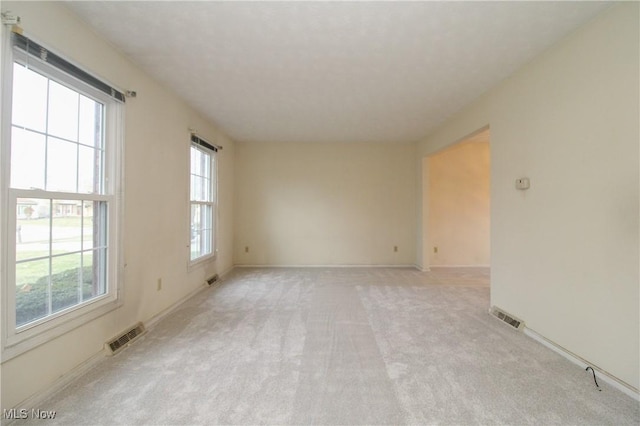 unfurnished room with a healthy amount of sunlight, visible vents, and light carpet