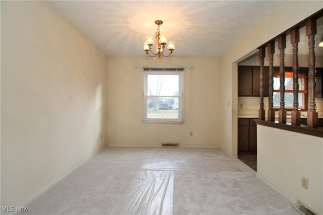 spare room featuring light carpet, visible vents, a chandelier, and baseboards