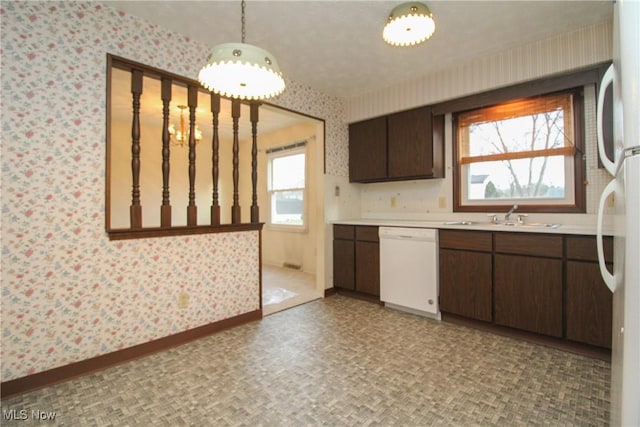 kitchen with wallpapered walls, white appliances, baseboards, light countertops, and a sink