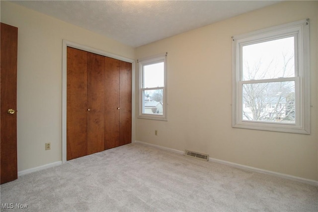 unfurnished bedroom with baseboards, visible vents, a textured ceiling, carpet floors, and a closet