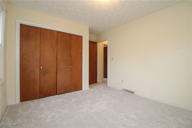 unfurnished bedroom with a textured ceiling, a closet, carpet flooring, and visible vents