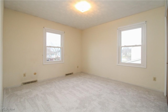 empty room with a healthy amount of sunlight, carpet floors, and visible vents