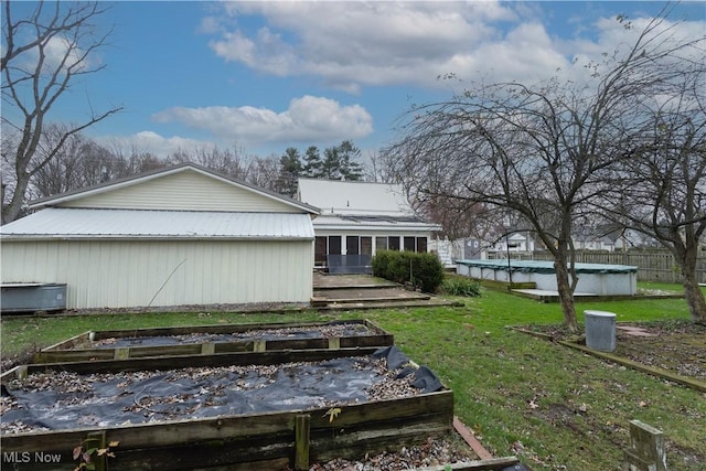 back of house featuring metal roof, fence, a lawn, a vegetable garden, and a covered pool