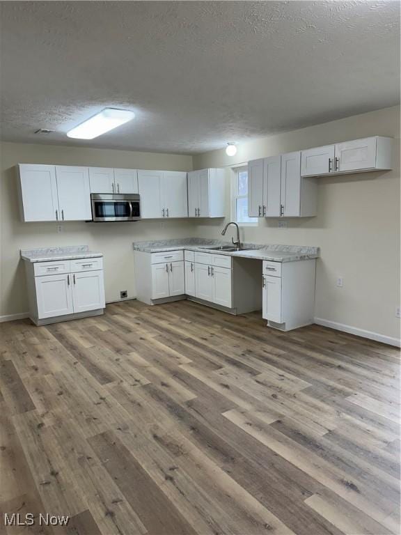 kitchen featuring stainless steel microwave, a sink, a textured ceiling, wood finished floors, and baseboards