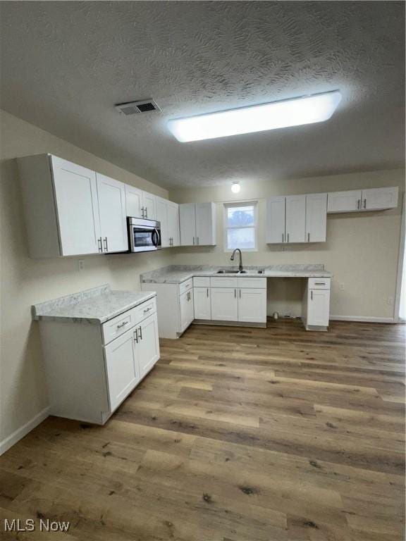 kitchen featuring visible vents, stainless steel microwave, wood finished floors, white cabinetry, and a sink