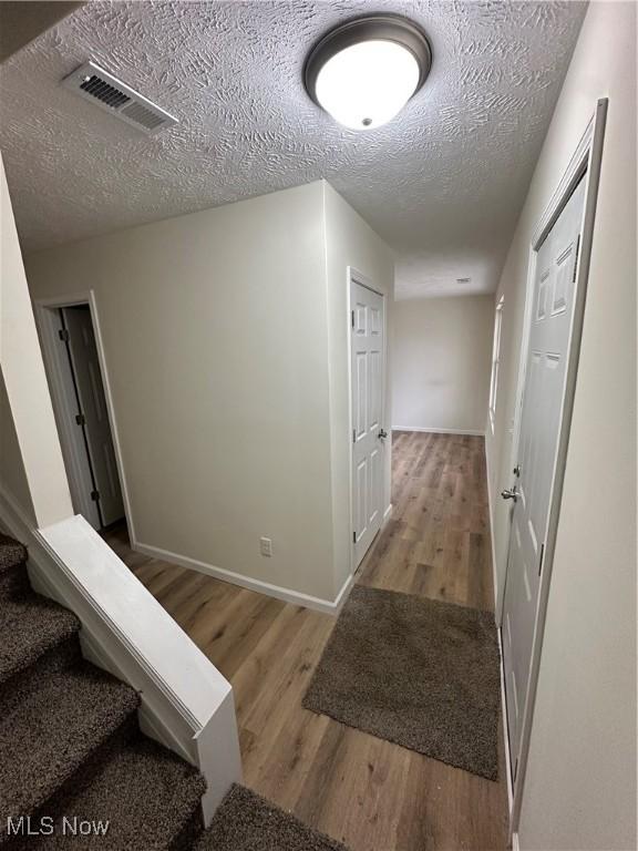 hall with visible vents, stairway, a textured ceiling, wood finished floors, and baseboards