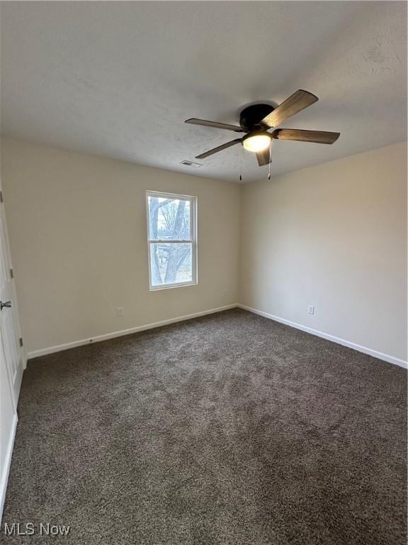 empty room with ceiling fan, dark colored carpet, visible vents, and baseboards