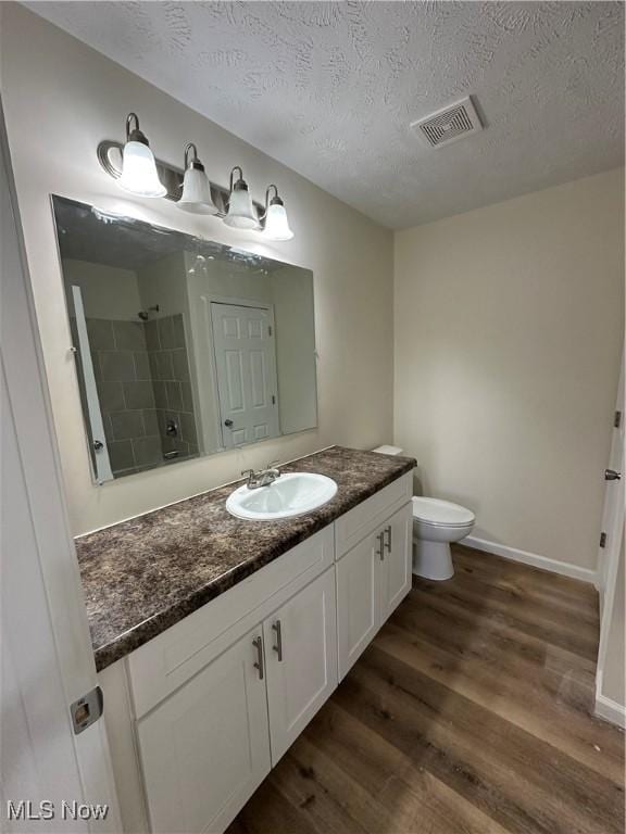 bathroom featuring visible vents, toilet, vanity, wood finished floors, and walk in shower