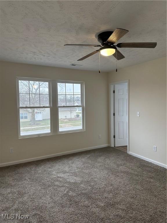 unfurnished room featuring carpet, visible vents, a ceiling fan, a textured ceiling, and baseboards