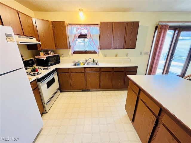 kitchen featuring white appliances, light floors, light countertops, under cabinet range hood, and a sink