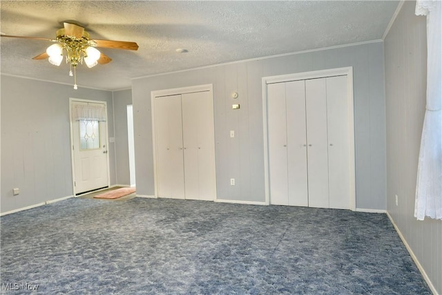 unfurnished bedroom with a textured ceiling, ornamental molding, carpet flooring, and multiple closets