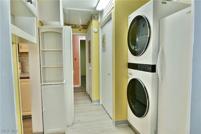 washroom with laundry area, baseboards, light wood-style floors, stacked washing maching and dryer, and attic access