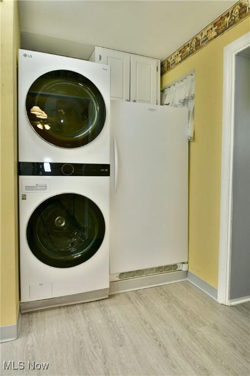 clothes washing area with stacked washer and dryer, laundry area, baseboards, and wood finished floors