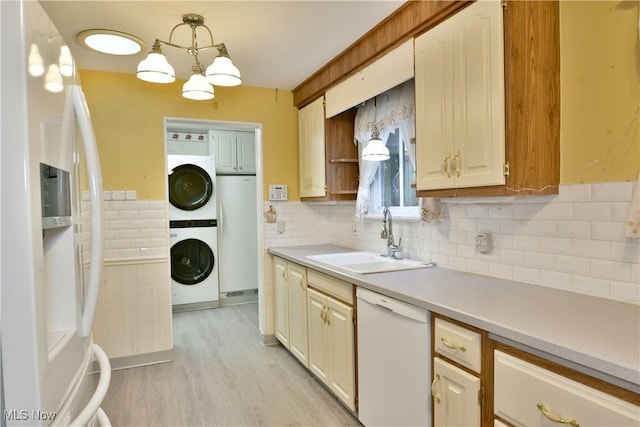 kitchen featuring pendant lighting, stacked washer and dryer, light countertops, a sink, and white appliances