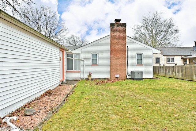 rear view of house featuring cooling unit, fence, a chimney, and a lawn