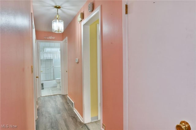 hall with visible vents, baseboards, and wood finished floors