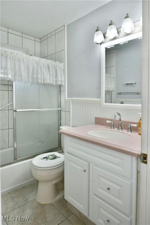 bathroom featuring bath / shower combo with glass door, wainscoting, toilet, tile patterned floors, and vanity