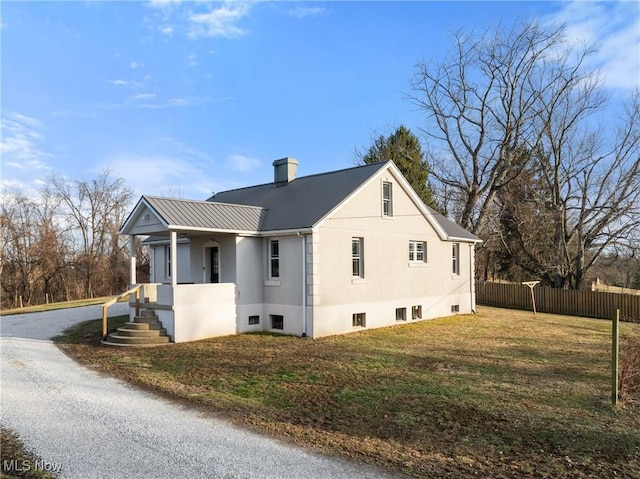 view of side of home with metal roof, a lawn, fence, and stucco siding